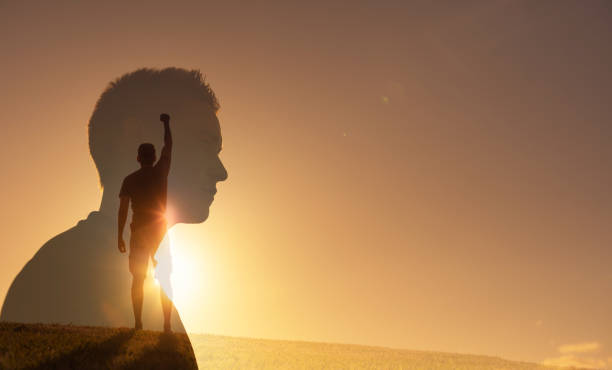 A man standing on a hill at sunrise confidently holds his fist up in the air.